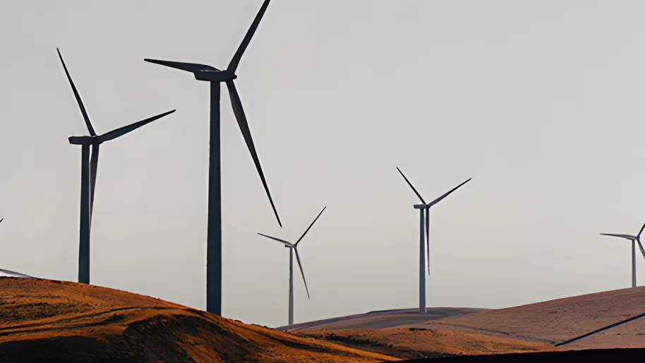 Wind turbines standing along a bare ridge under a pale, flat sky.