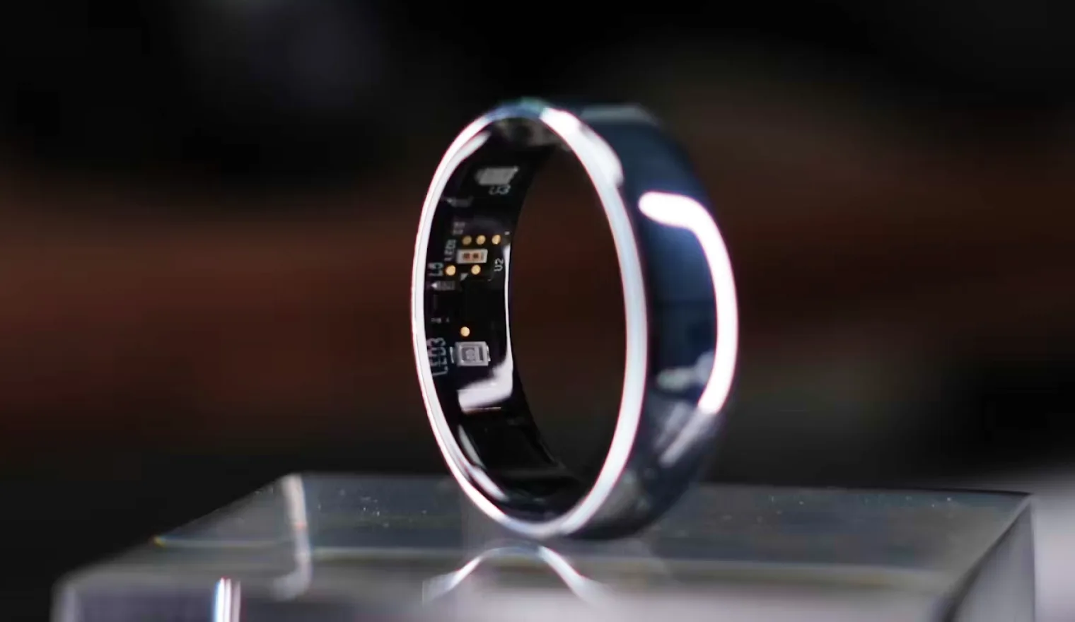 A smart ring standing on a clear pedestal, the sensors on its inner side in view, the room behind it out of focus.